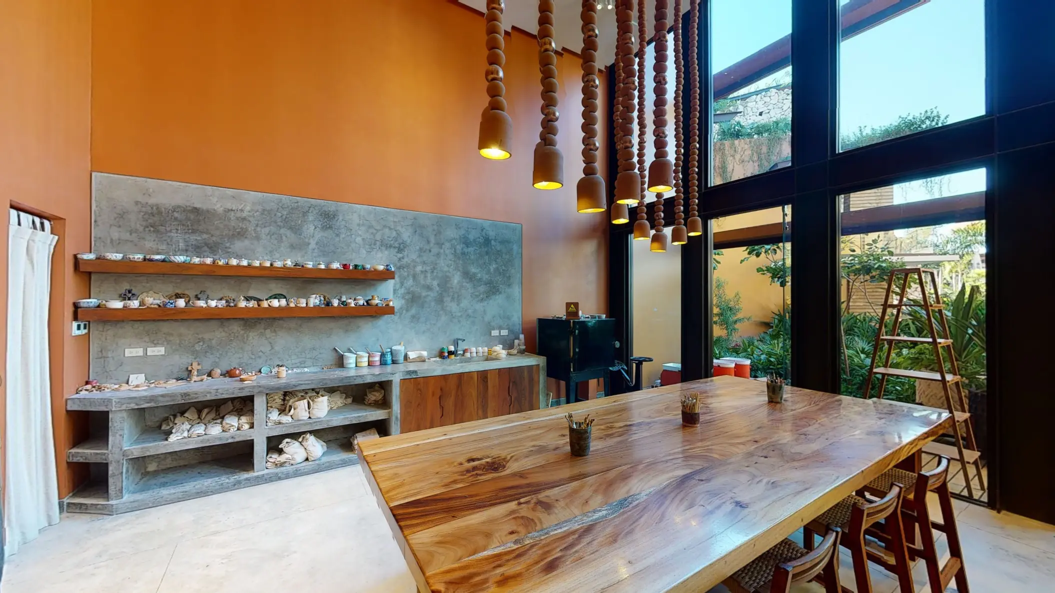 Artistic workshop room with pottery tools, natural wood table, terracotta pendant lights, and garden views.