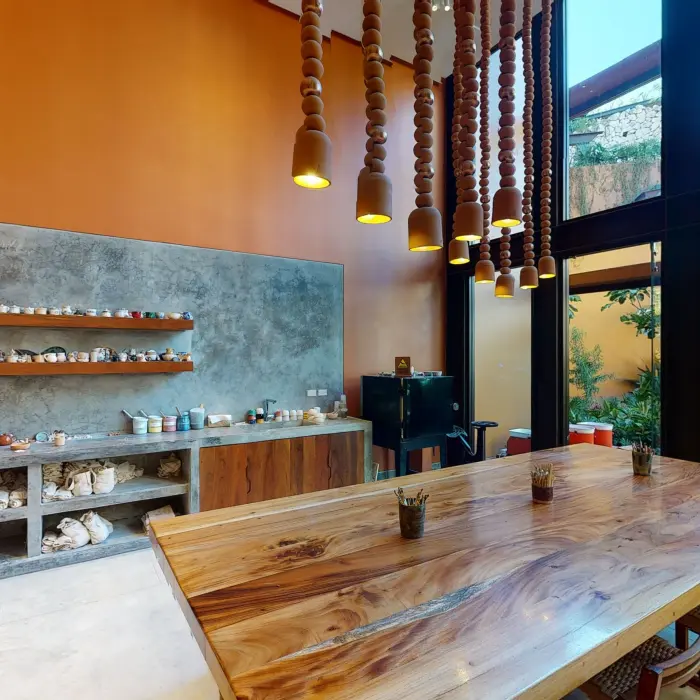 Artistic workshop room with pottery tools, natural wood table, terracotta pendant lights, and garden views.