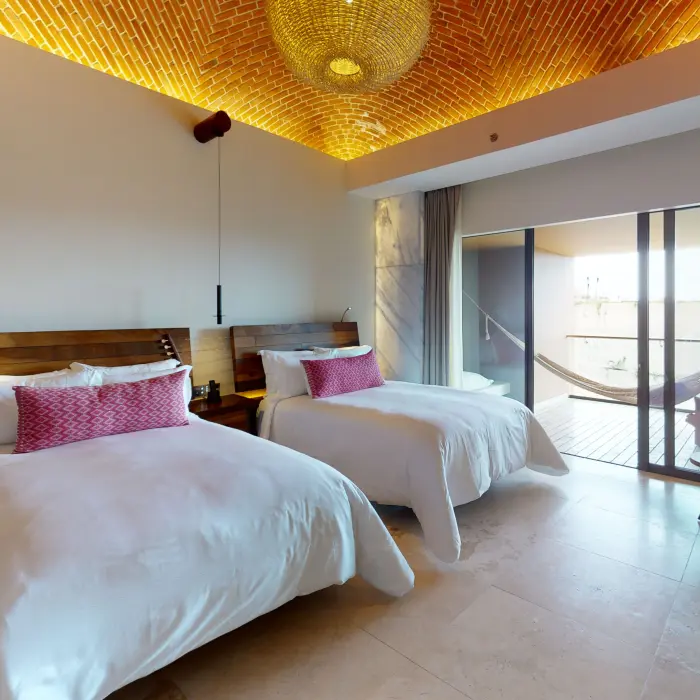 Spacious modern guest room with two queen beds, vaulted brick ceiling, and balcony hammock.