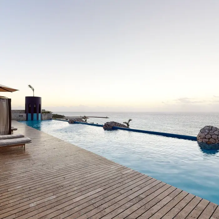 Infinity pool facing the Caribbean Sea with shaded loungers and serene ocean horizon at dusk.