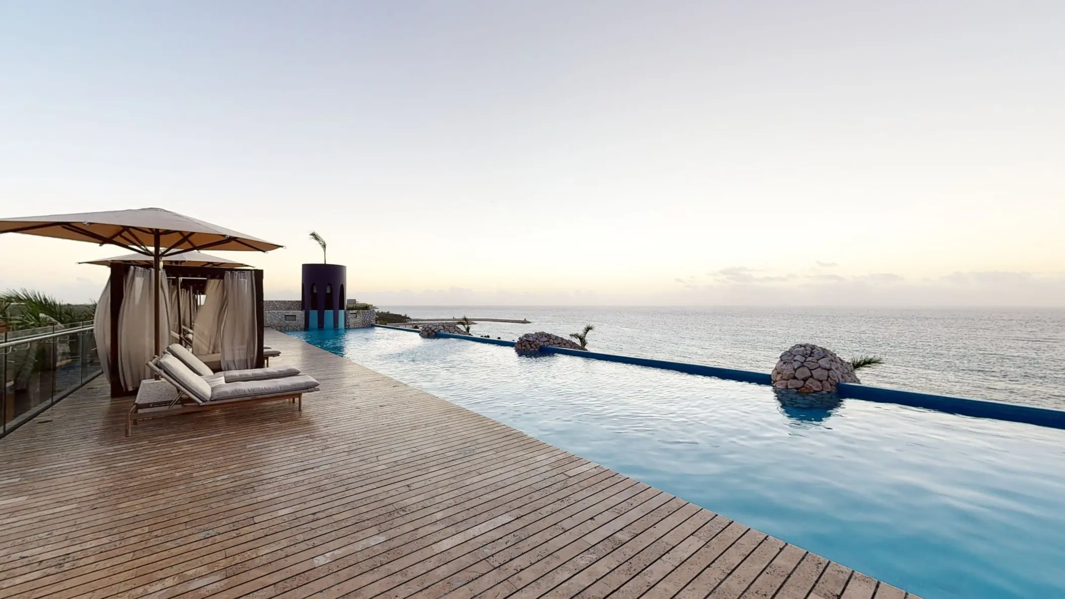 Infinity pool facing the Caribbean Sea with shaded loungers and serene ocean horizon at dusk.