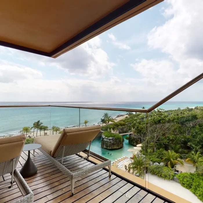 Private terrace with cushioned loungers overlooking turquoise ocean and lush greenery.