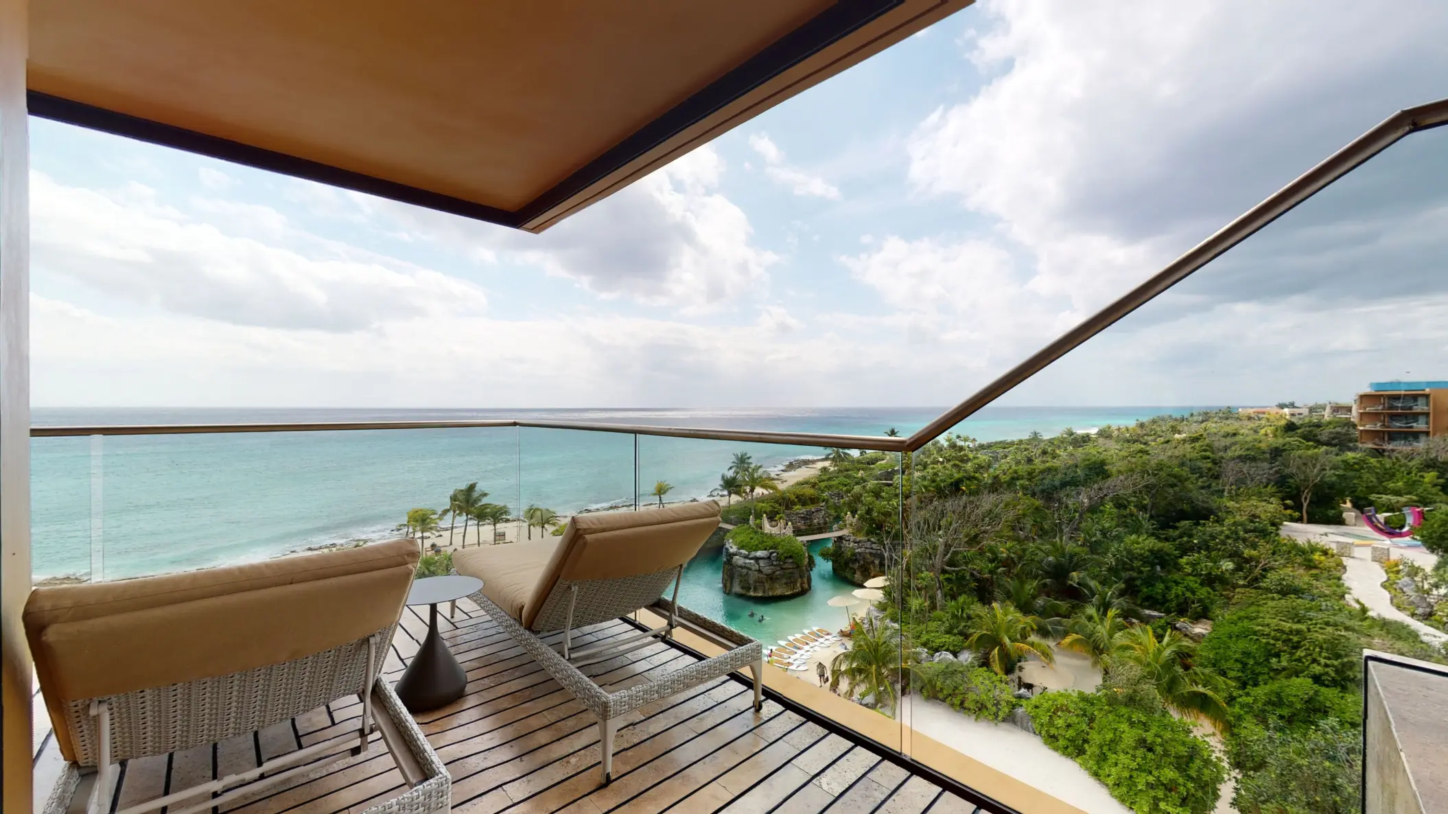 Private terrace with cushioned loungers overlooking turquoise ocean and lush greenery.