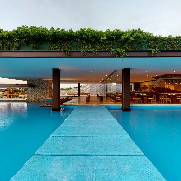 Walkway across infinity pool leading to open-air restaurant with lush rooftop garden.