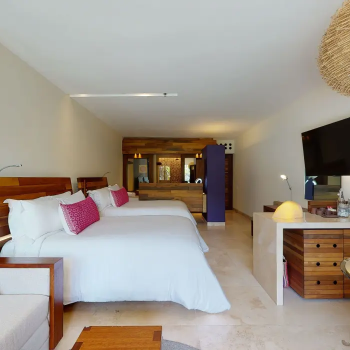 Spacious hotel room with two queen beds, warm lighting, and wood furnishings.