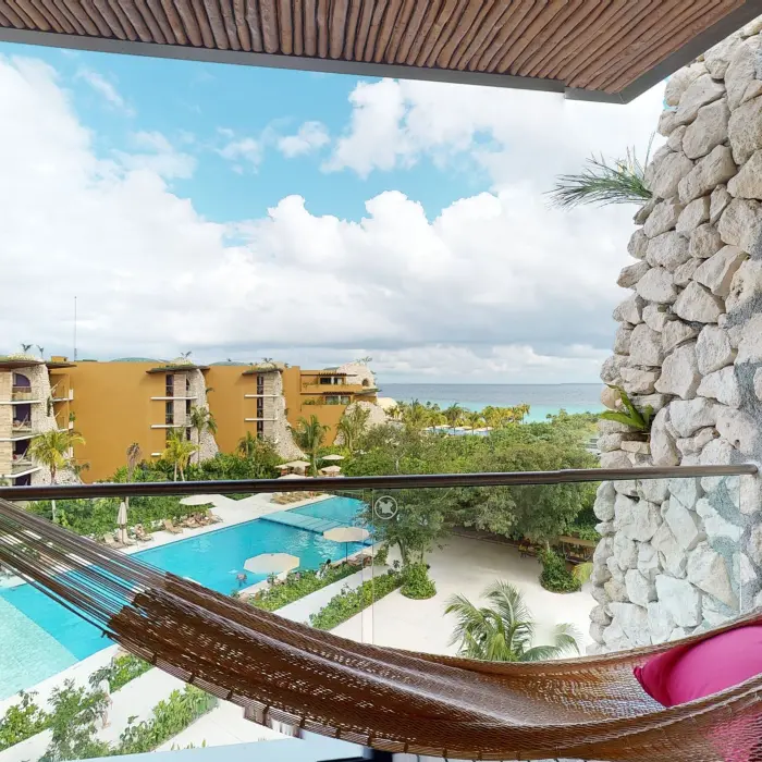 Private balcony with hammock overlooking pool and yellow-toned hotel buildings.