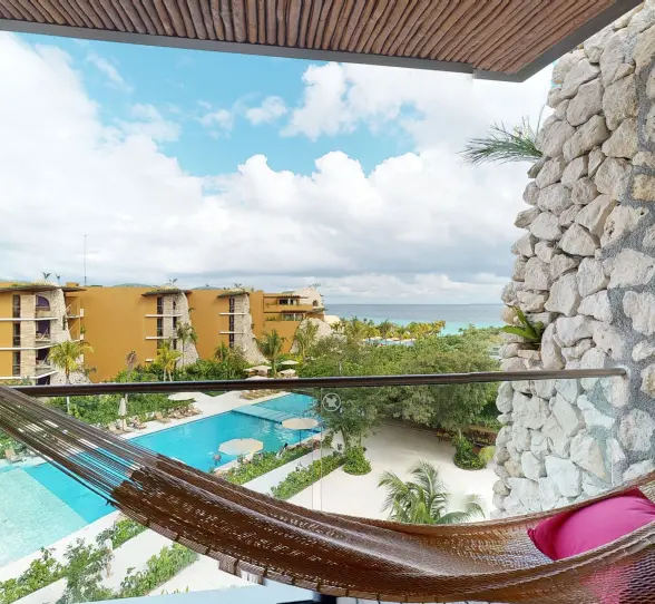 Private balcony with hammock overlooking pool and yellow-toned hotel buildings.