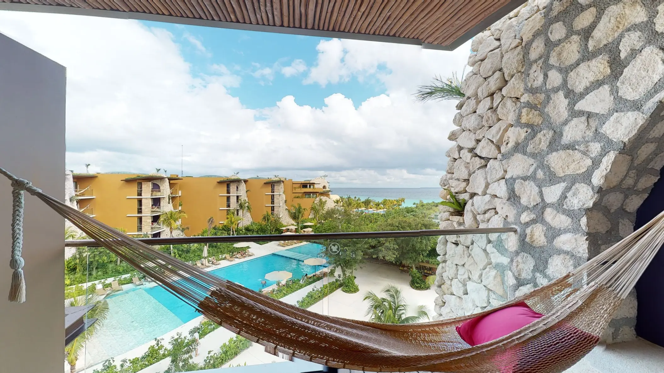 Private balcony with hammock overlooking pool and yellow-toned hotel buildings.