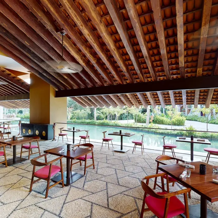 Open-air restaurant with canal views, rustic ceiling beams, and red-accented chairs.