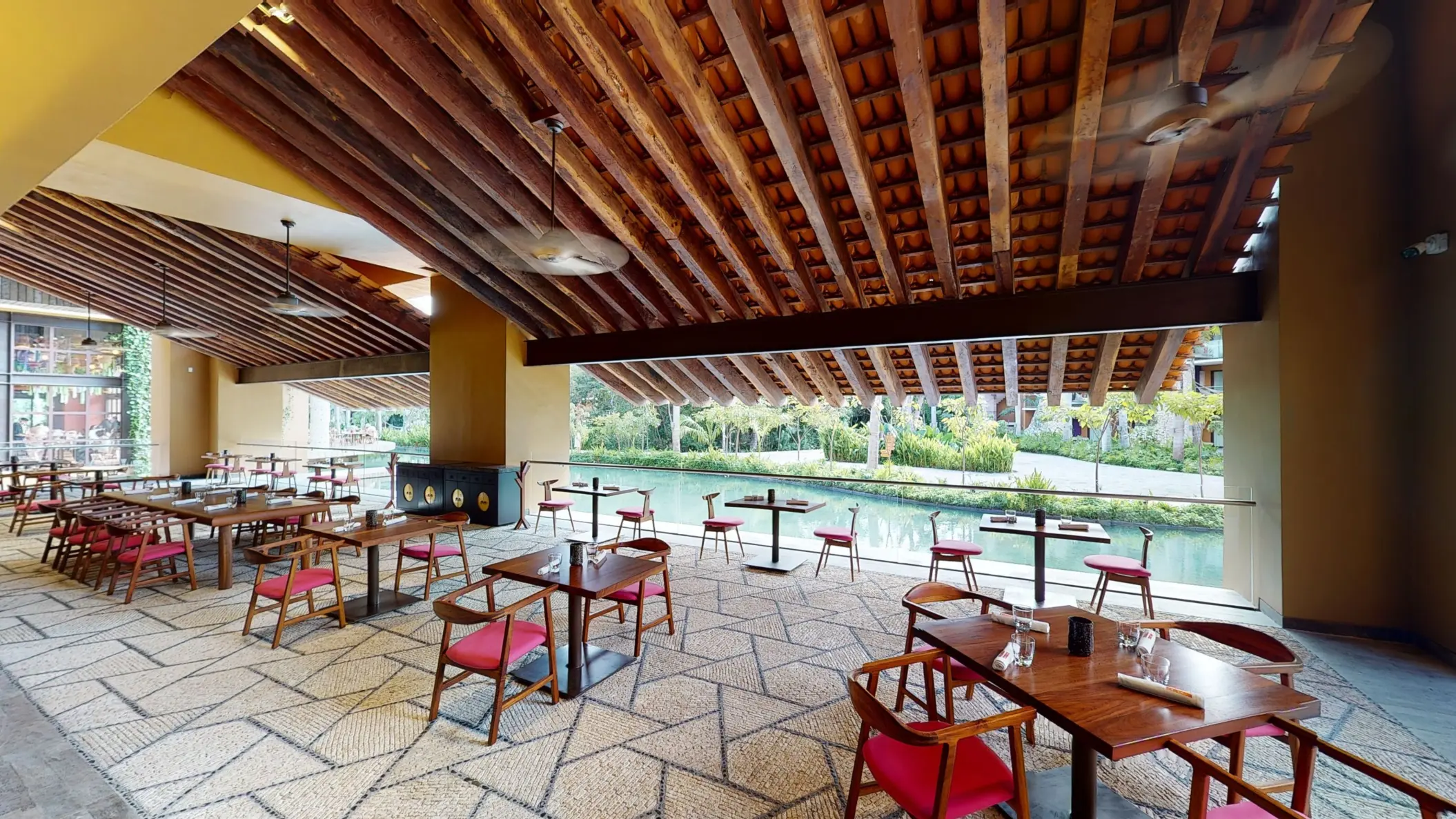 Open-air restaurant with canal views, rustic ceiling beams, and red-accented chairs.