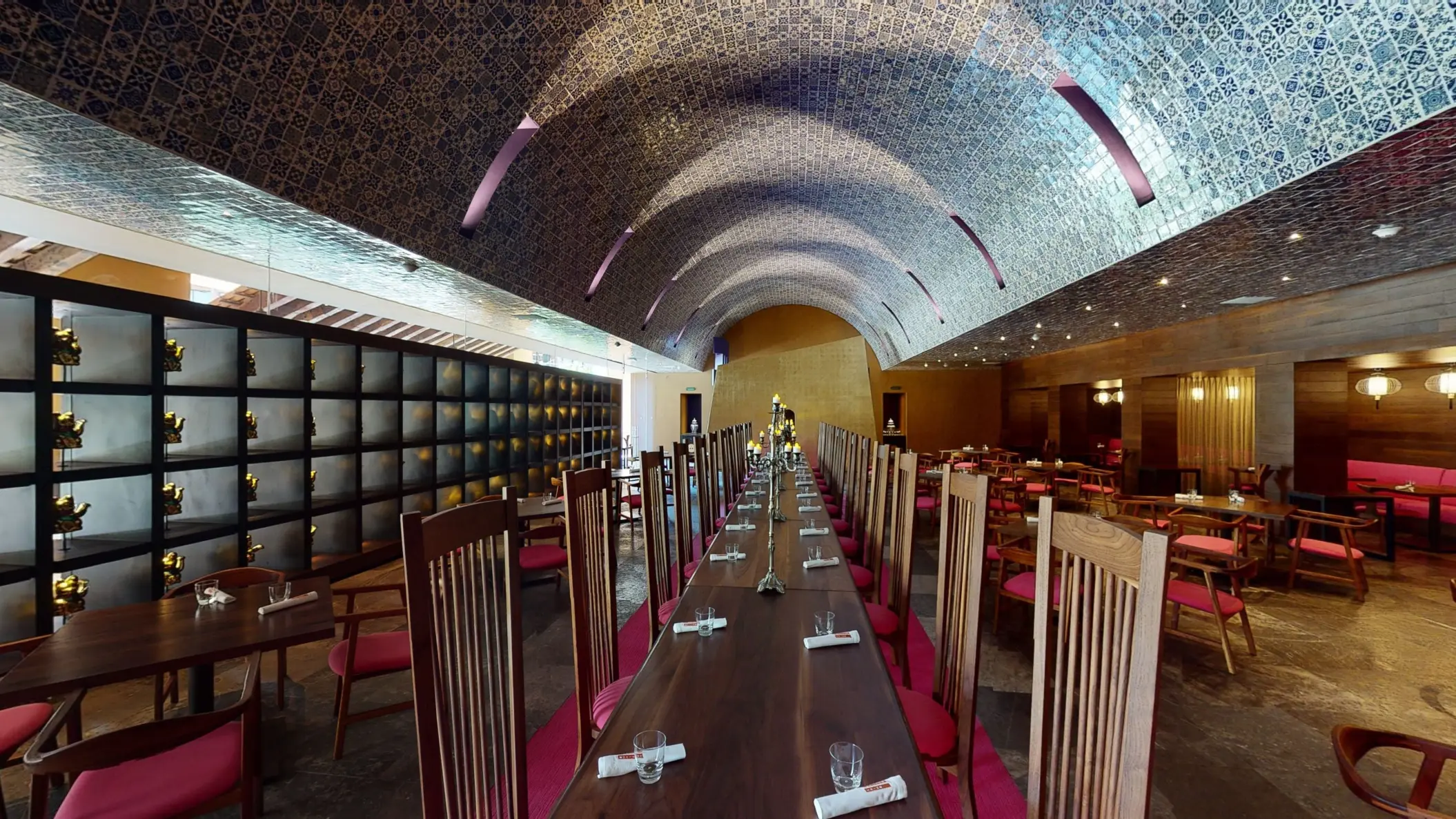 Long communal dining table under arched blue tile ceiling with elegant ambiance.