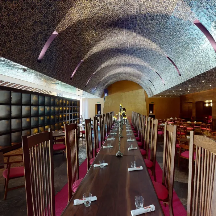 Long communal dining table under arched blue tile ceiling with elegant ambiance.