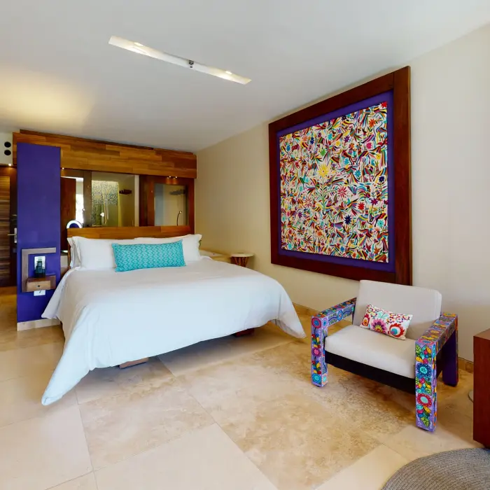 Modern guest room with king bed, colorful Otomi-inspired artwork, and cozy seating area with turquoise pillows.