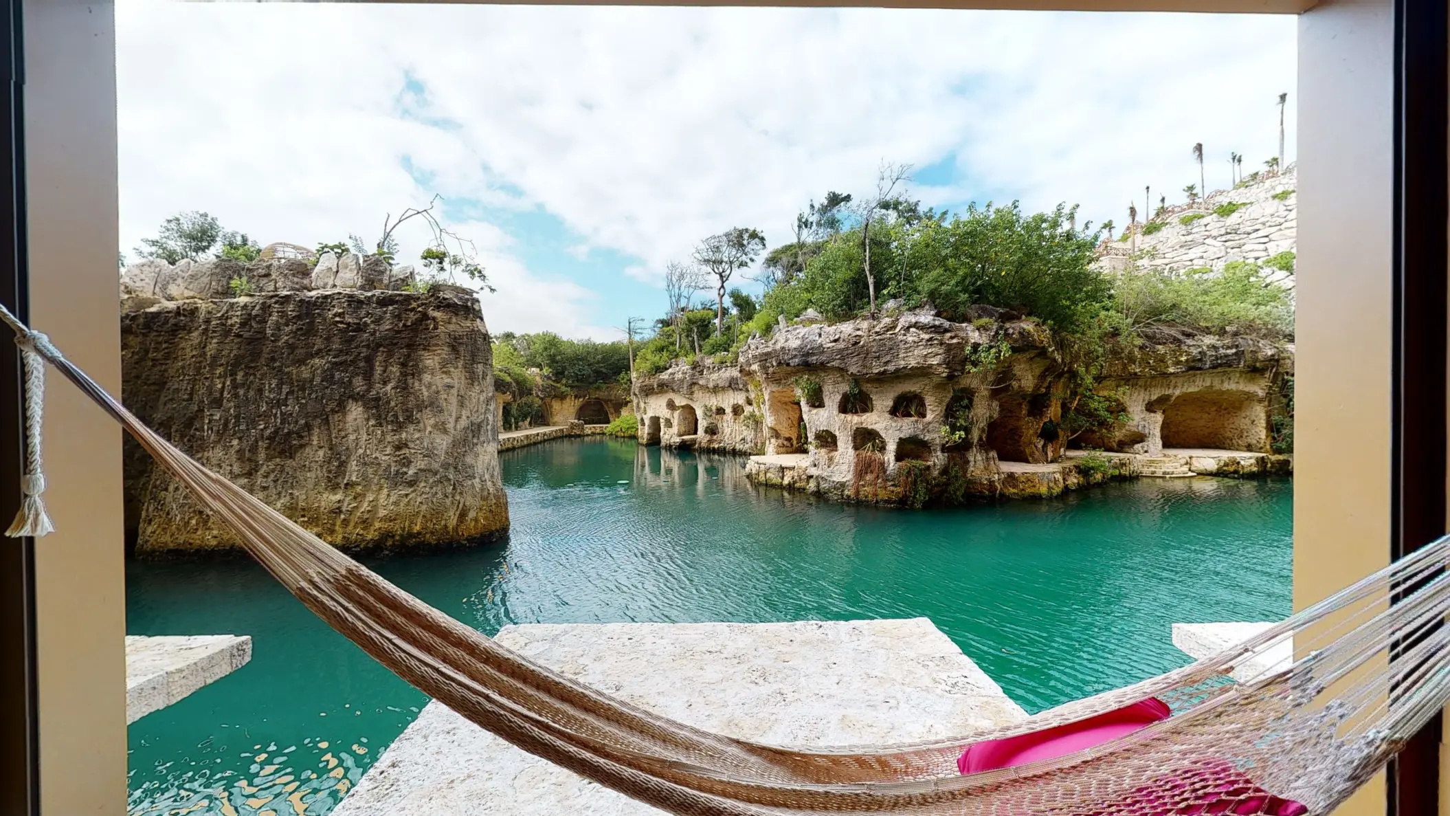 Hammock hanging over turquoise river view with natural rock formations and lush jungle surroundings at Hotel Xcaret Arte.