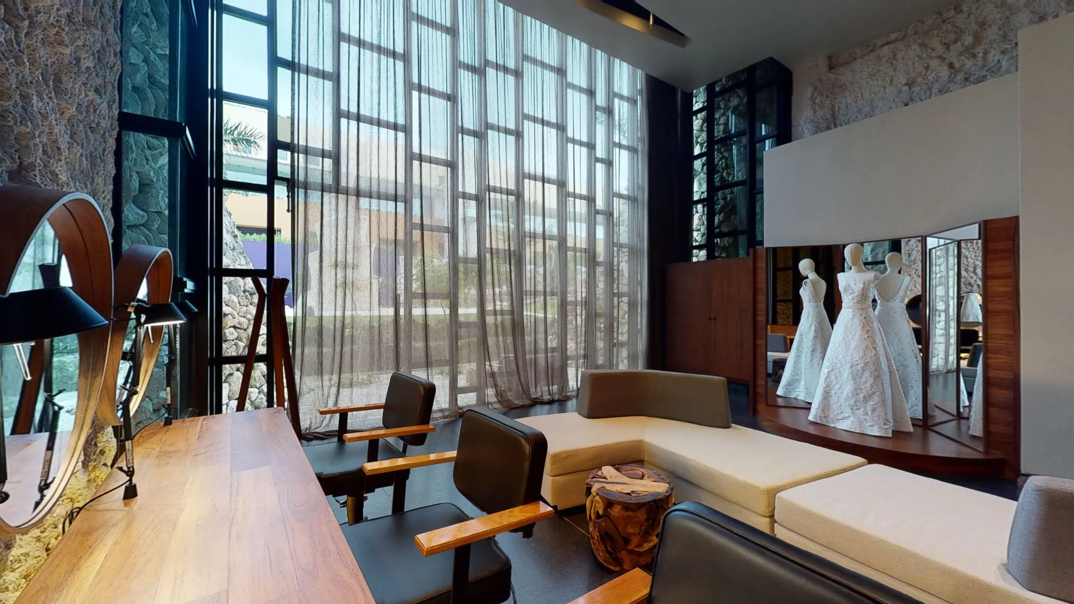 Bridal lounge with wedding dresses on display, makeup stations, and large windows at Hotel Xcaret Arte's beauty salon.