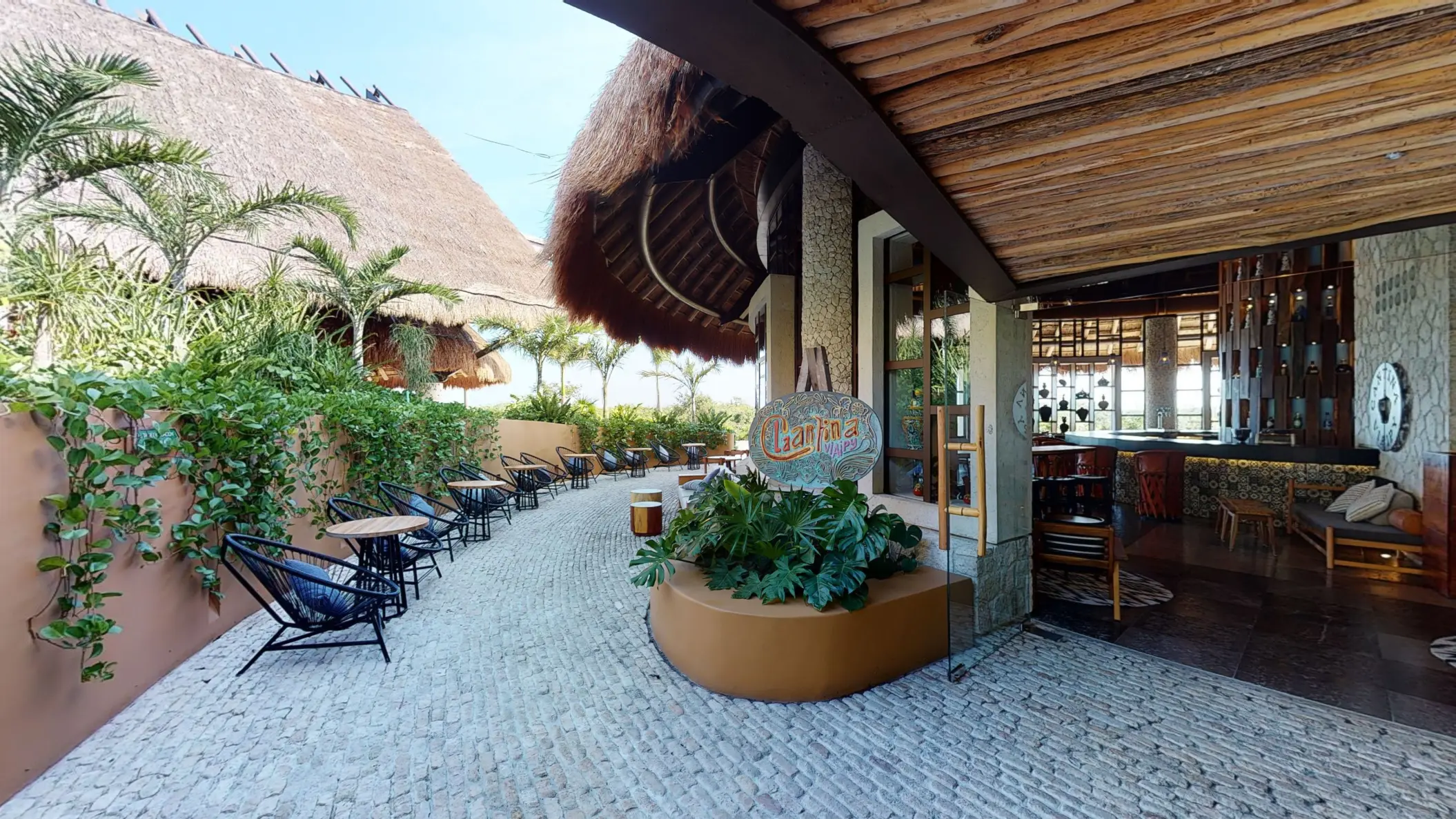Cantina V.I.A.I.P.Y entrance with outdoor seating area with tropical plants & cobblestone floor.