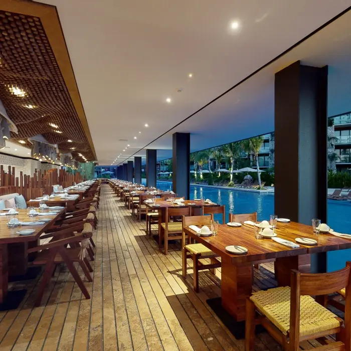 Open-air restaurant at Hotel Xcaret Arte with wood furnishings and views of the river-style pool.