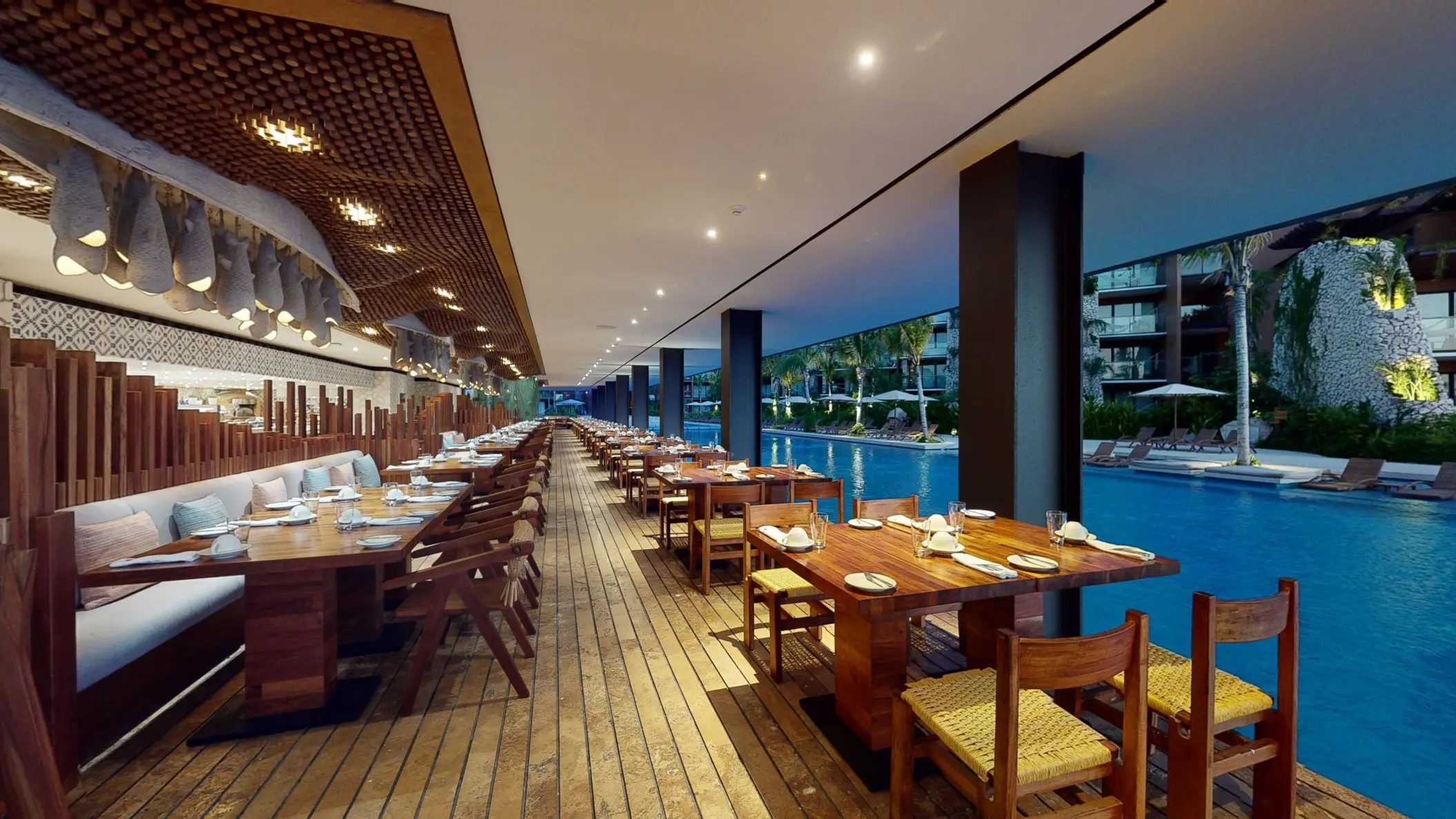 Open-air restaurant at Hotel Xcaret Arte with wood furnishings and views of the river-style pool.