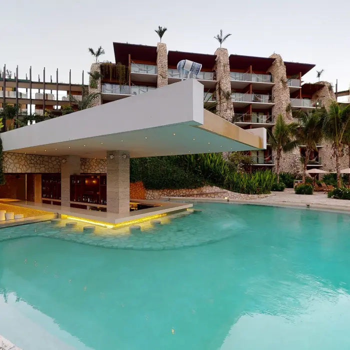 Swim-up bar surrounded by lush greenery and rustic architecture at Hotel Xcaret Arte.