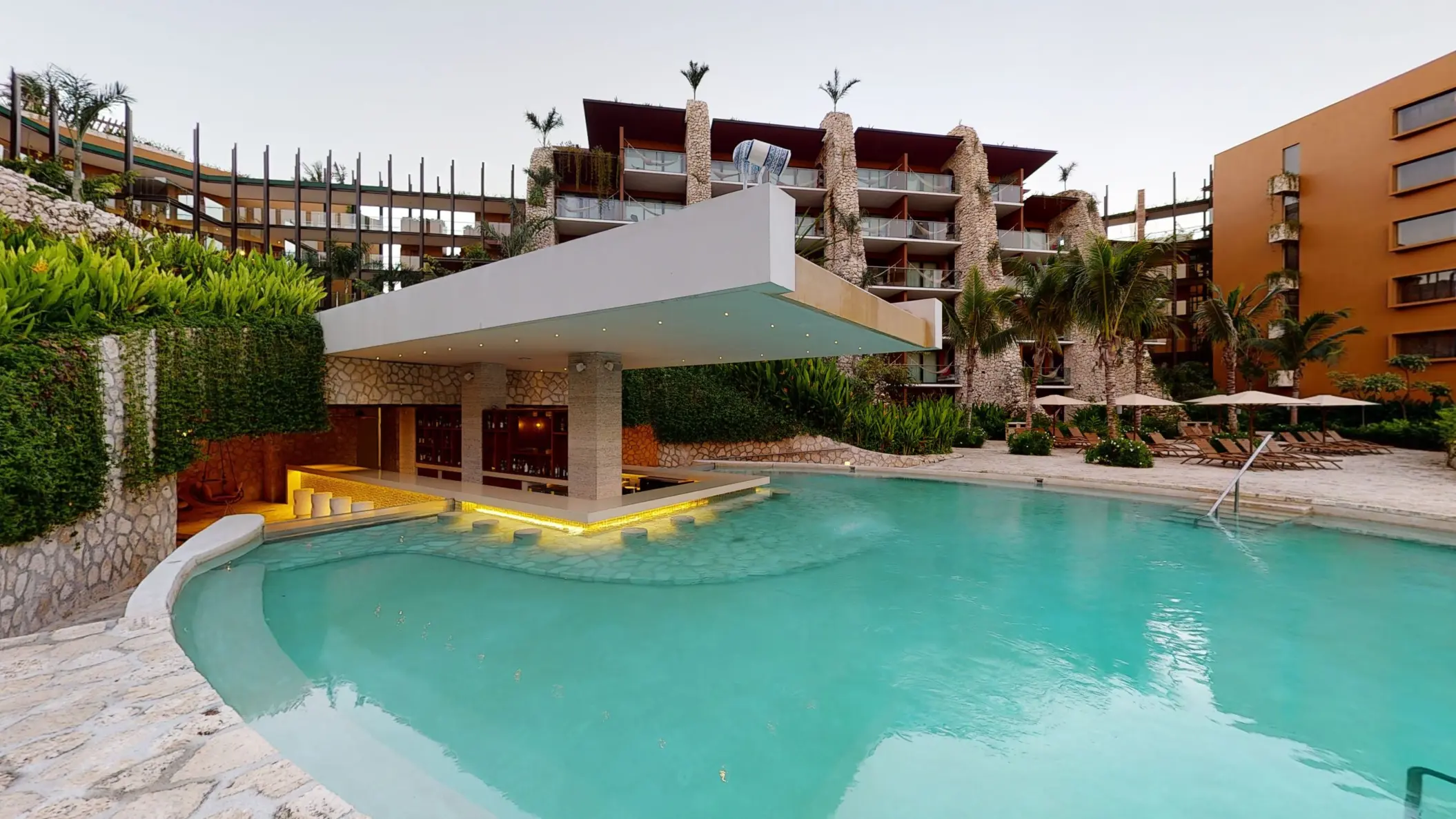 Swim-up bar surrounded by lush greenery and rustic architecture at Hotel Xcaret Arte.
