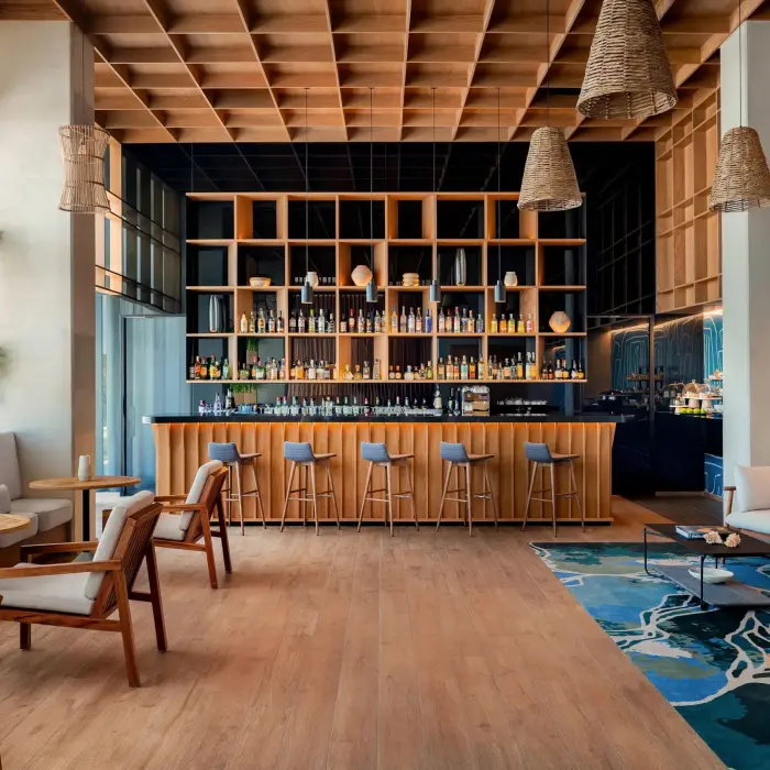 Upscale indoor lounge bar with wooden ceiling, stylish furniture, greenery, and floor-to-ceiling bottle display.