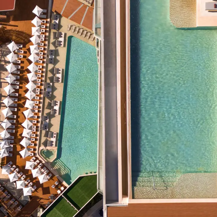 Split aerial view of large pool deck with rows of loungers, umbrellas, and modern geometric stepping stones.
