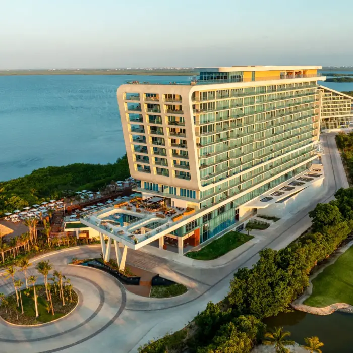 Modern beachfront resort surrounded by golf course and lagoon, captured at golden hour with warm light.