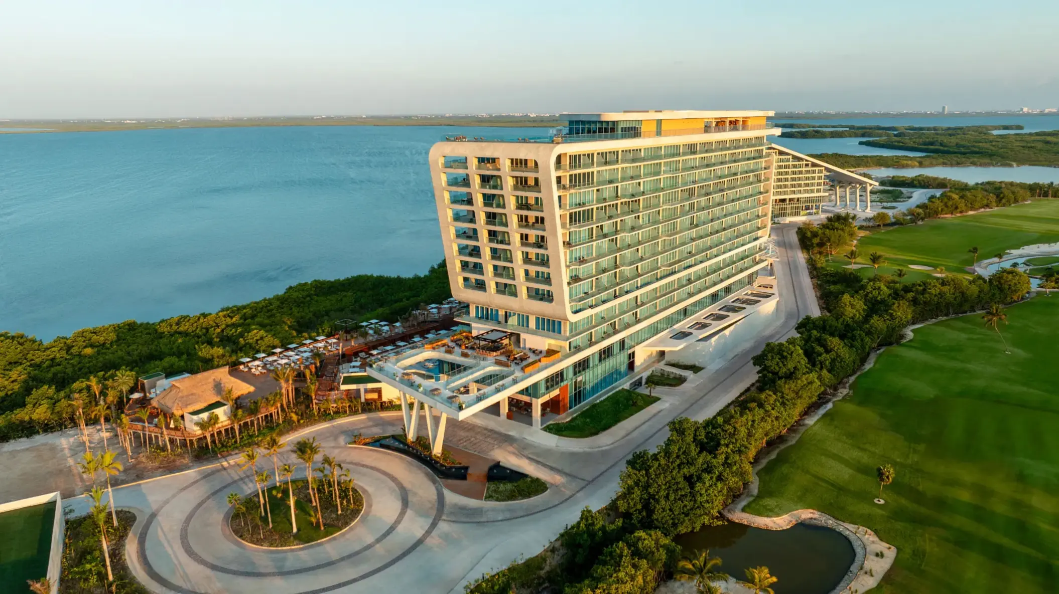 Modern beachfront resort surrounded by golf course and lagoon, captured at golden hour with warm light.