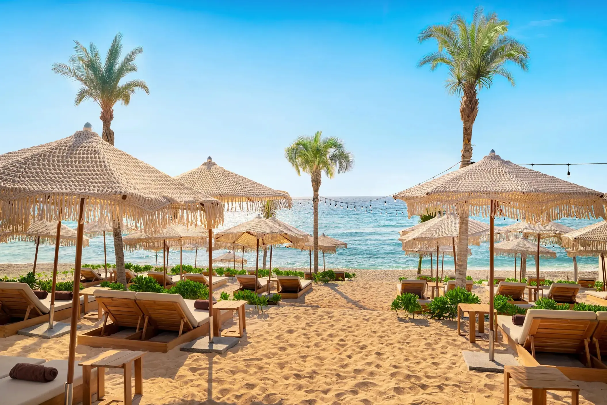White sand beach with woven umbrellas, wooden loungers, and palm trees facing turquoise ocean waters.