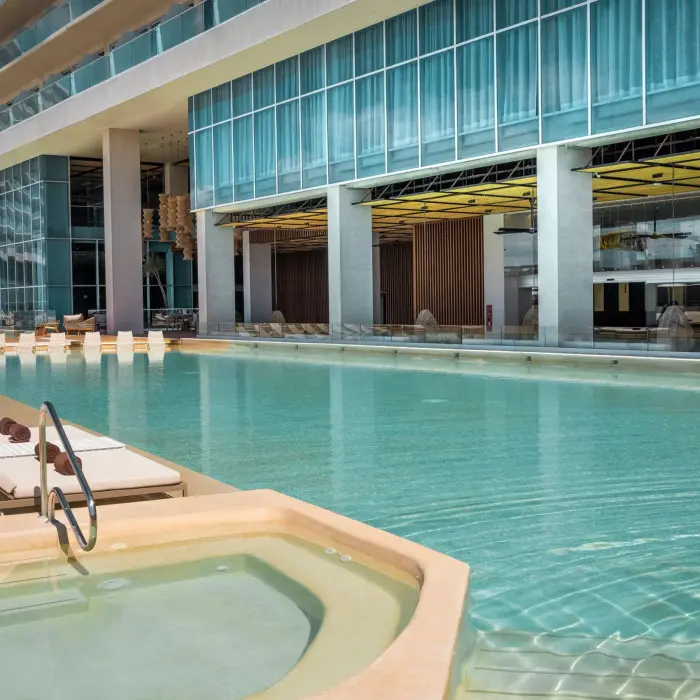 Long pool lined with white loungers, a hot tub, and modern resort exterior with open-air design.