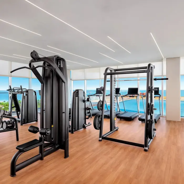 Modern fitness center with cardio equipment, free weights, and jungle views through floor-to-ceiling windows.