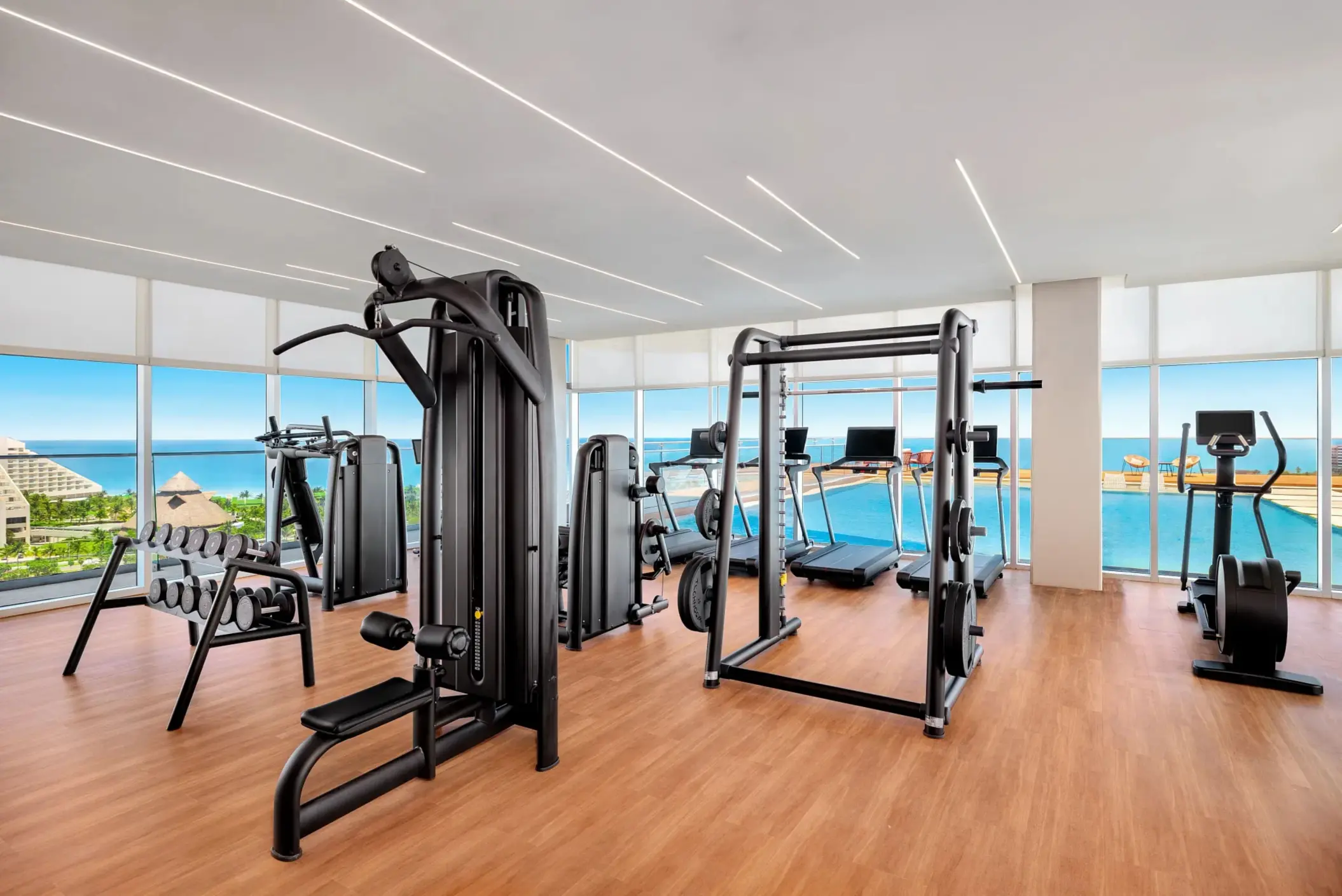 Modern fitness center with cardio equipment, free weights, and jungle views through floor-to-ceiling windows.