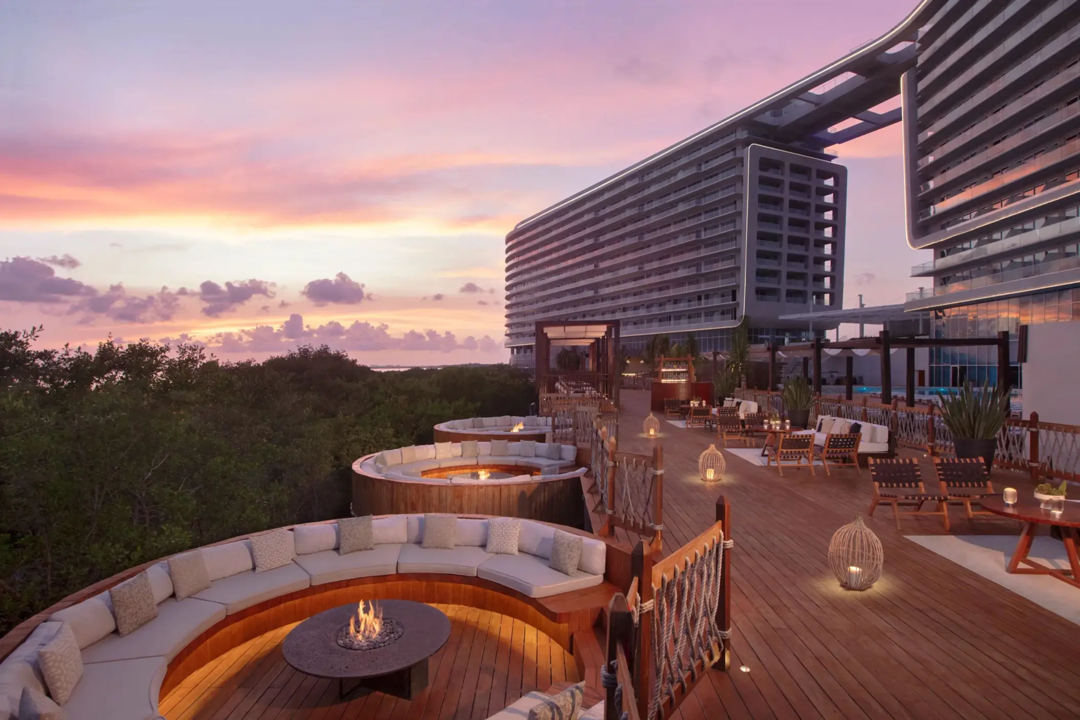Outdoor cocktail space with modern fire pits, cozy seating, and views of tropical greenery at dusk.
