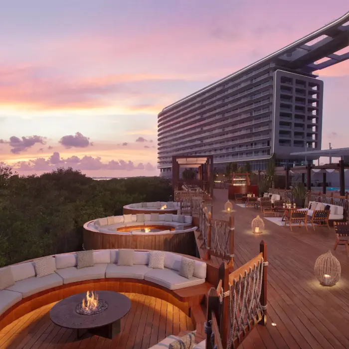 Outdoor cocktail space with modern fire pits, cozy seating, and views of tropical greenery at dusk.