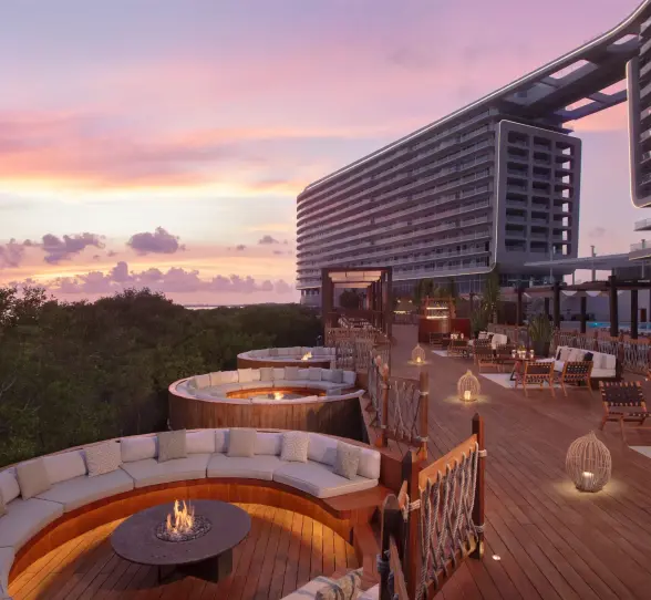 Outdoor cocktail space with modern fire pits, cozy seating, and views of tropical greenery at dusk.