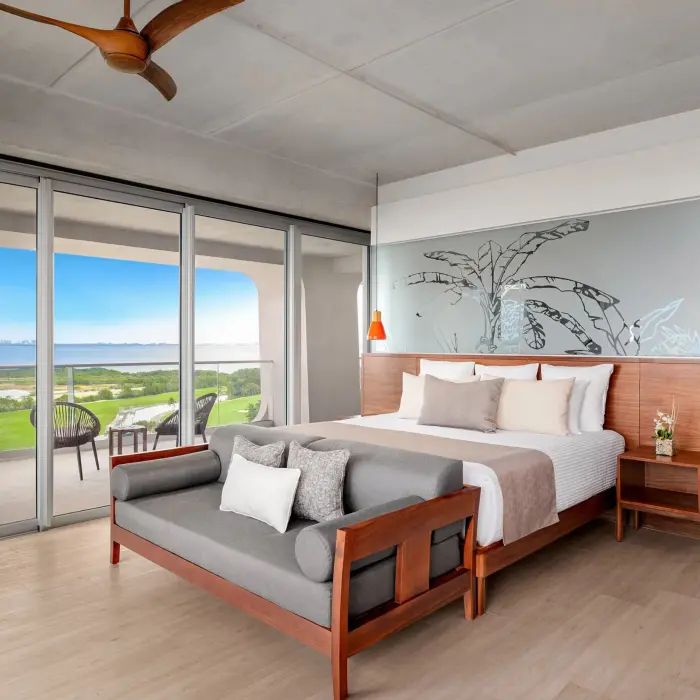 Spacious modern suite with king bed, wooden bench, and balcony overlooking lush greenery in Vantage Club section.