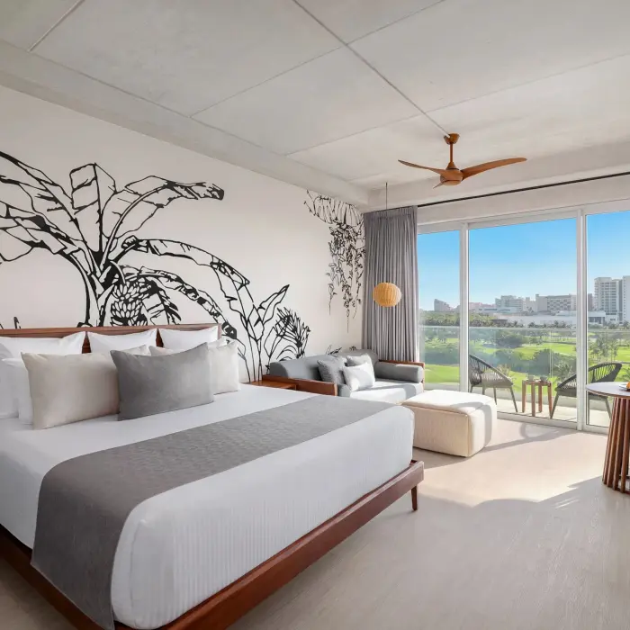Junior suite with king bed, sleek wood furnishings, and balcony overlooking golf course and greenery.