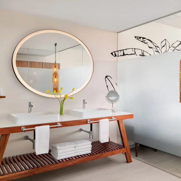 Modern junior suite bathroom with double vanities, round mirrors, and a freestanding soaking tub.