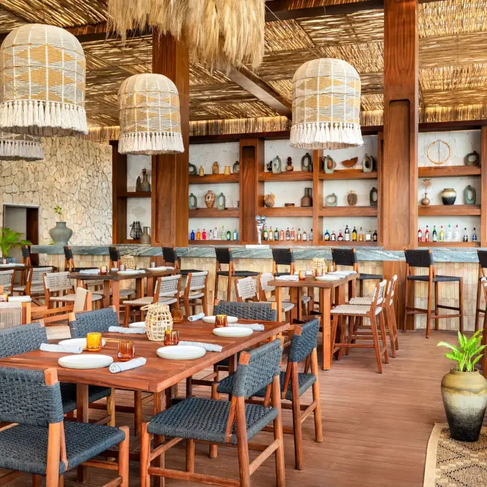 Rustic beach club restaurant with thatched ceiling, woven pendant lights, stone walls, and artisanal décor.
