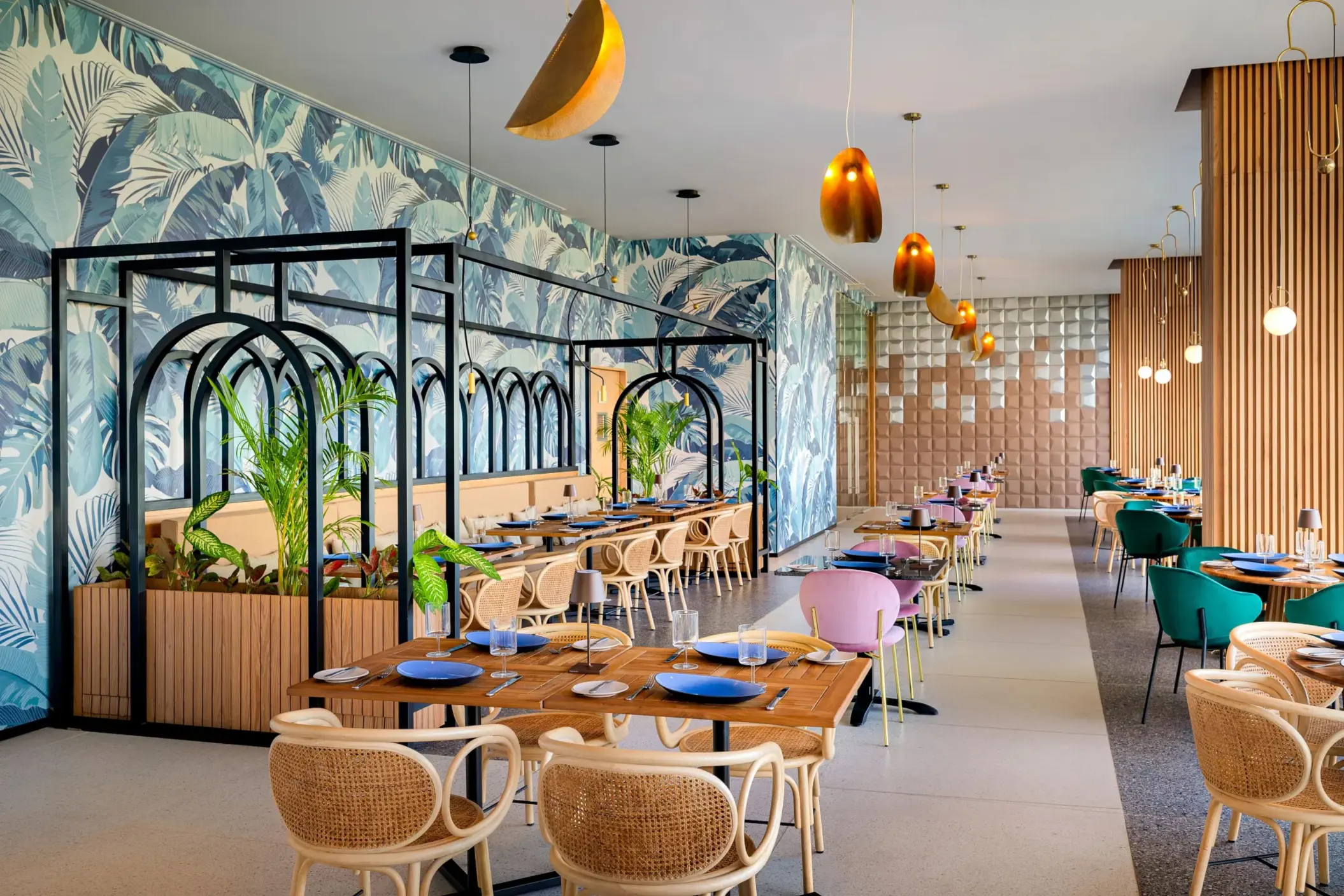 Vibrant dining space with botanical wallpaper, pastel chairs, and black arch dividers for a stylish ambiance.