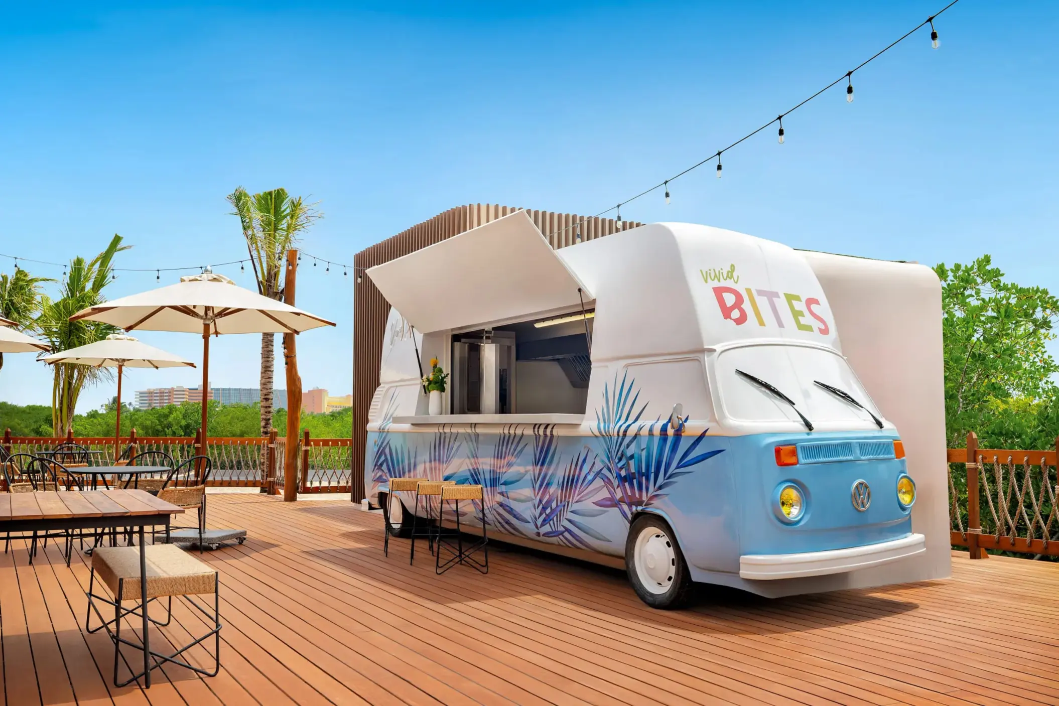 Colorful retro food truck labeled “Vivid Bites” on a sunny rooftop deck with string lights and palm trees.