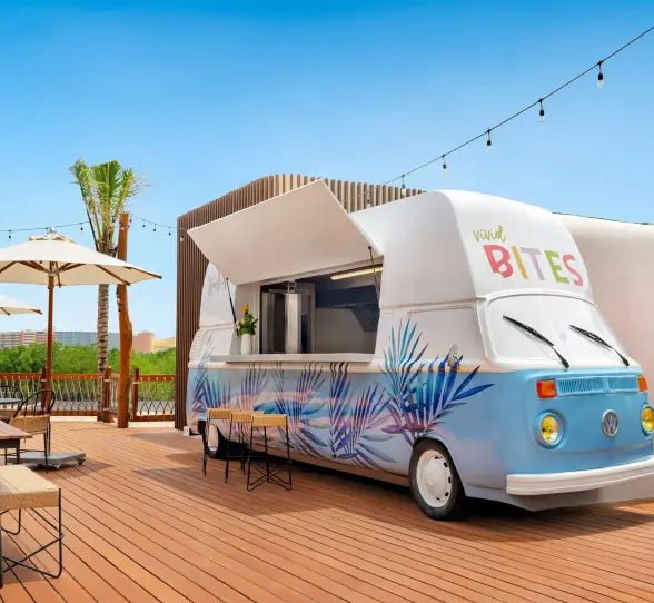 Colorful retro food truck labeled “Vivid Bites” on a sunny rooftop deck with string lights and palm trees.