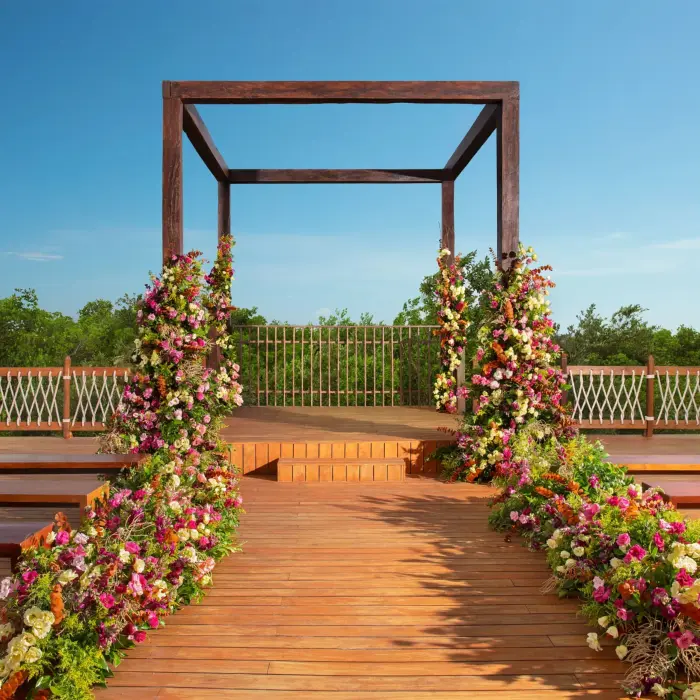 Outdoor wooden gazebo wedding setup with colorful floral aisle décor surrounded by tropical greenery and blue skies.