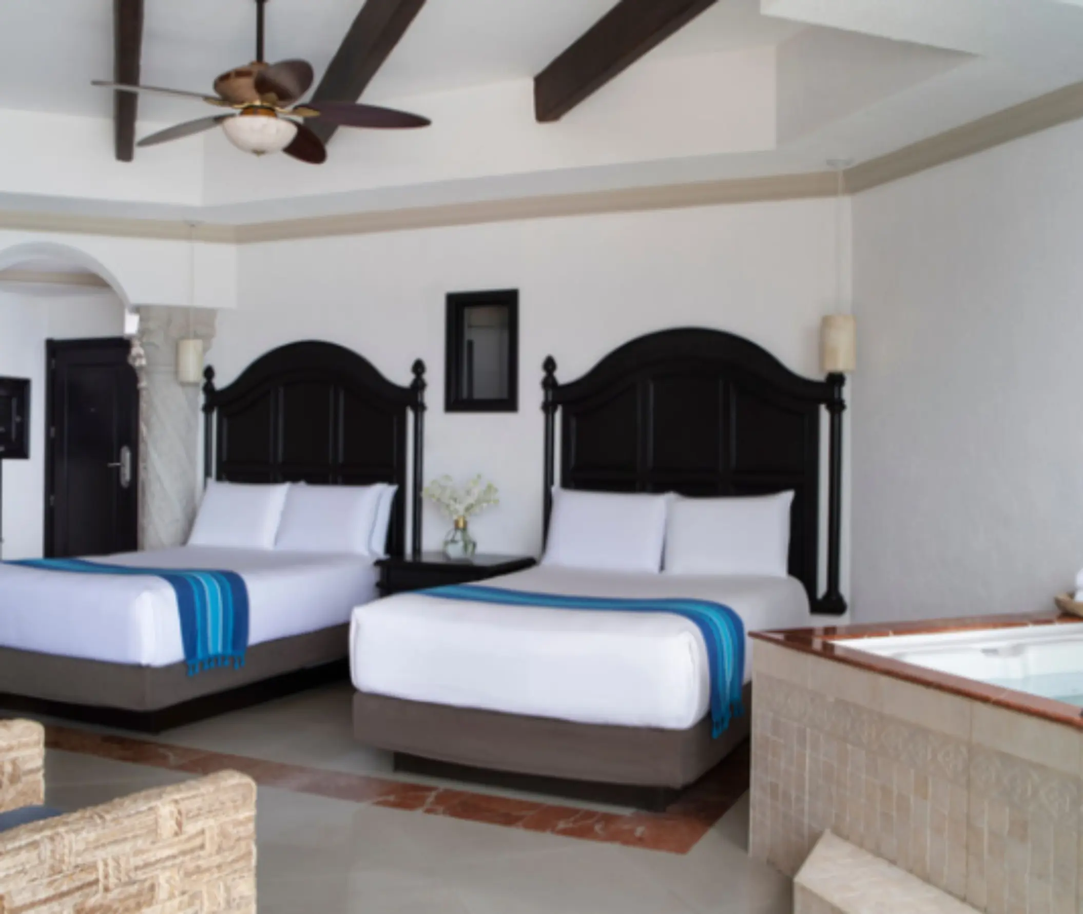 Spacious resort room with two queen beds, dark wood headboards, and a corner whirlpool tub beside a tiled floor.
