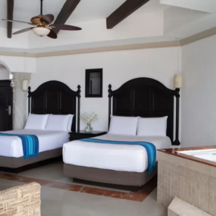Spacious resort room with two queen beds, dark wood headboards, and a corner whirlpool tub beside a tiled floor.