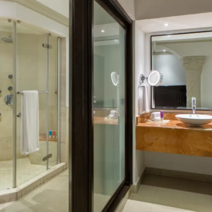 Modern resort bathroom with glass-enclosed shower, marble countertop, round sink, and large mirror near elegant lighting.