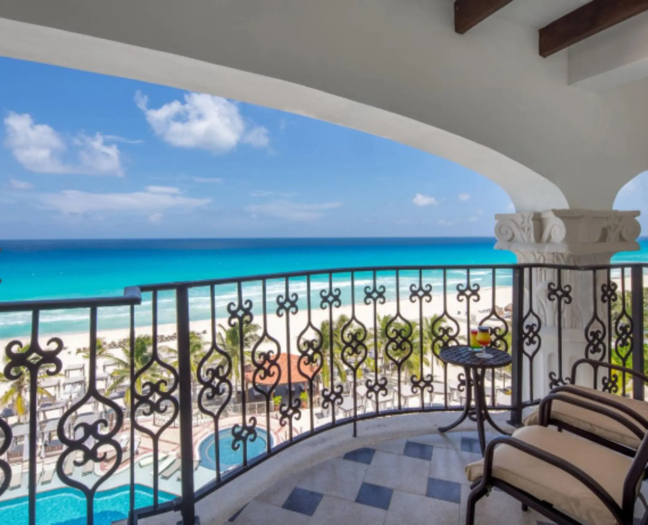 Oceanfront balcony with cushioned chairs and wrought-iron railings offering a clear view of the beach and pool area.