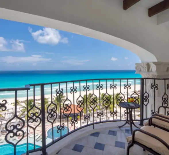Oceanfront balcony with cushioned chairs and wrought-iron railings offering a clear view of the beach and pool area.