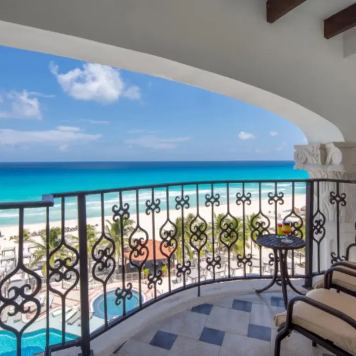 Oceanfront balcony with cushioned chairs and wrought-iron railings offering a clear view of the beach and pool area.