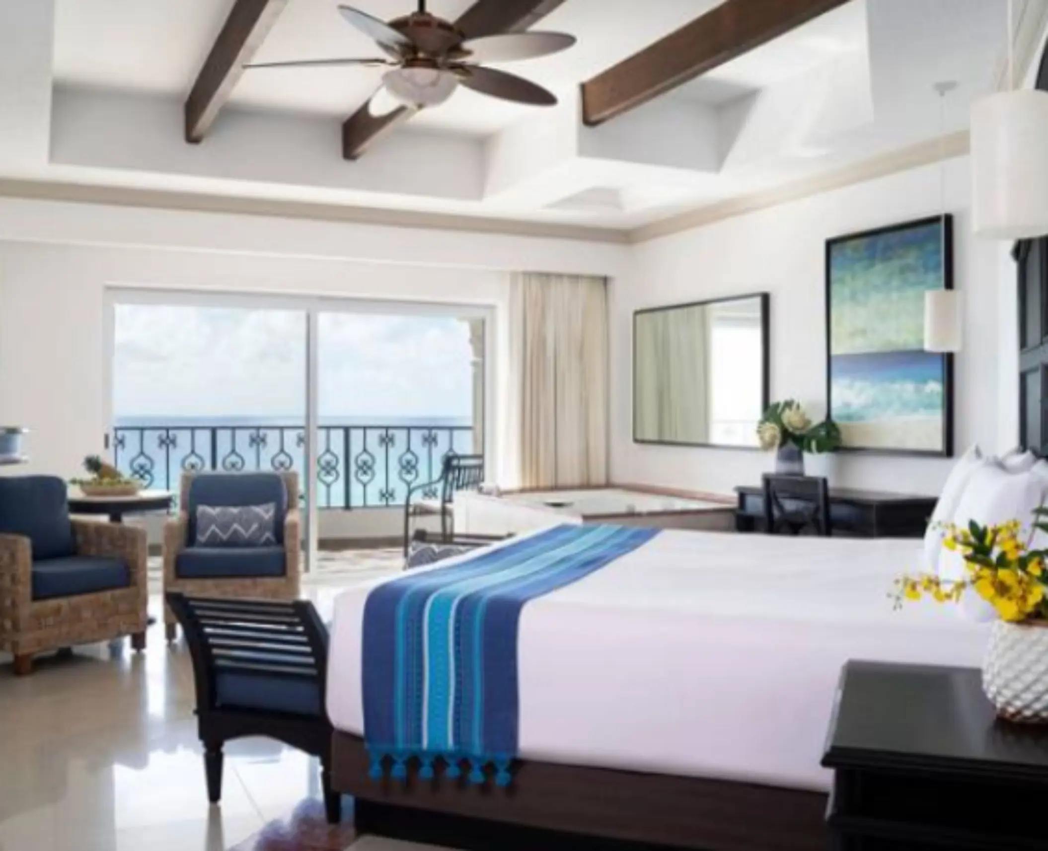 Bright oceanfront suite with king bed, cozy seating area, and glass doors to private balcony.